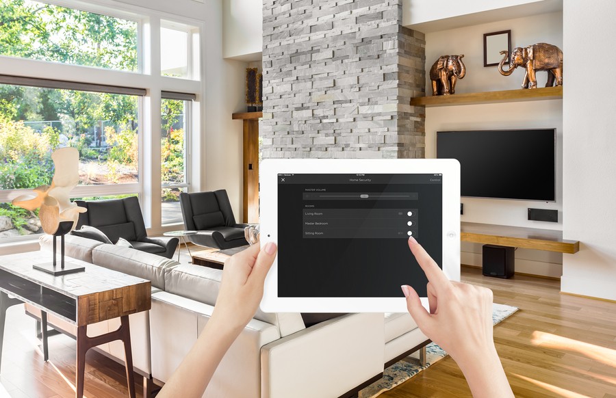 a hand holding a Savant control panel in a living room with glass windows and sofas.