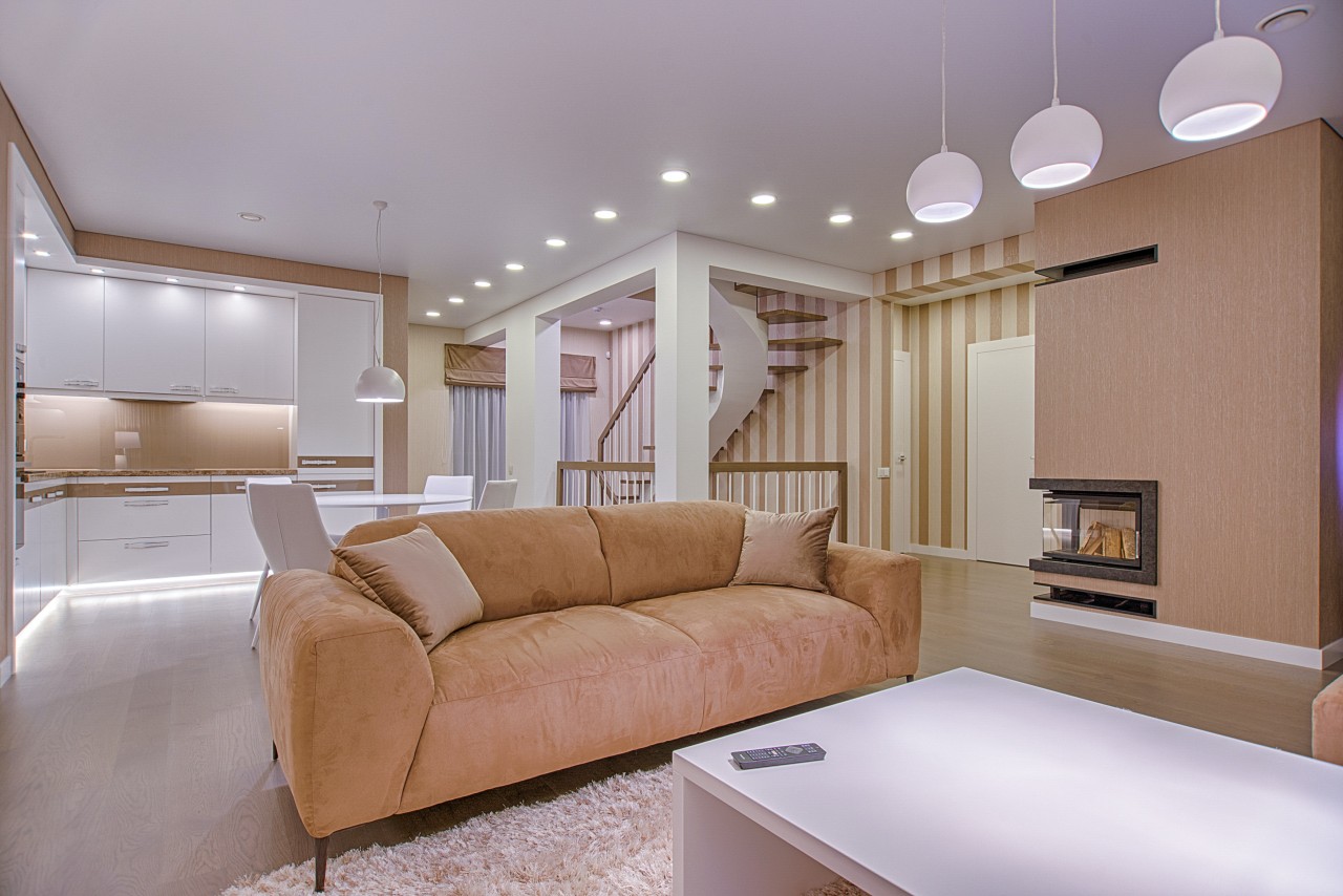 A beautiful living room featuring a couch, coffee table, and corner fireplace, well-lit with hanging fixtures and recessed lighting. 