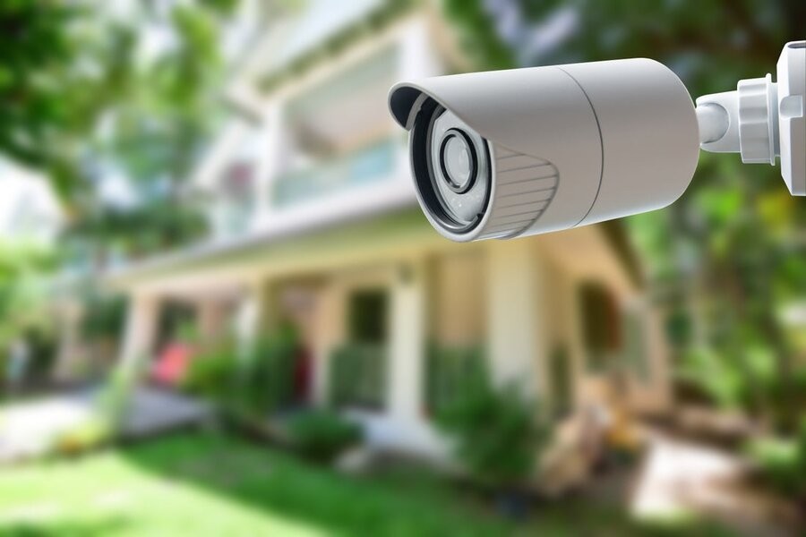 A smart surveillance camera in the foreground with a house in the background.