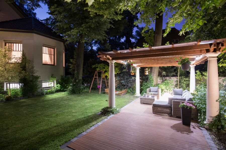 A pergola-covered gazebo in a backyard with a paved patio area.