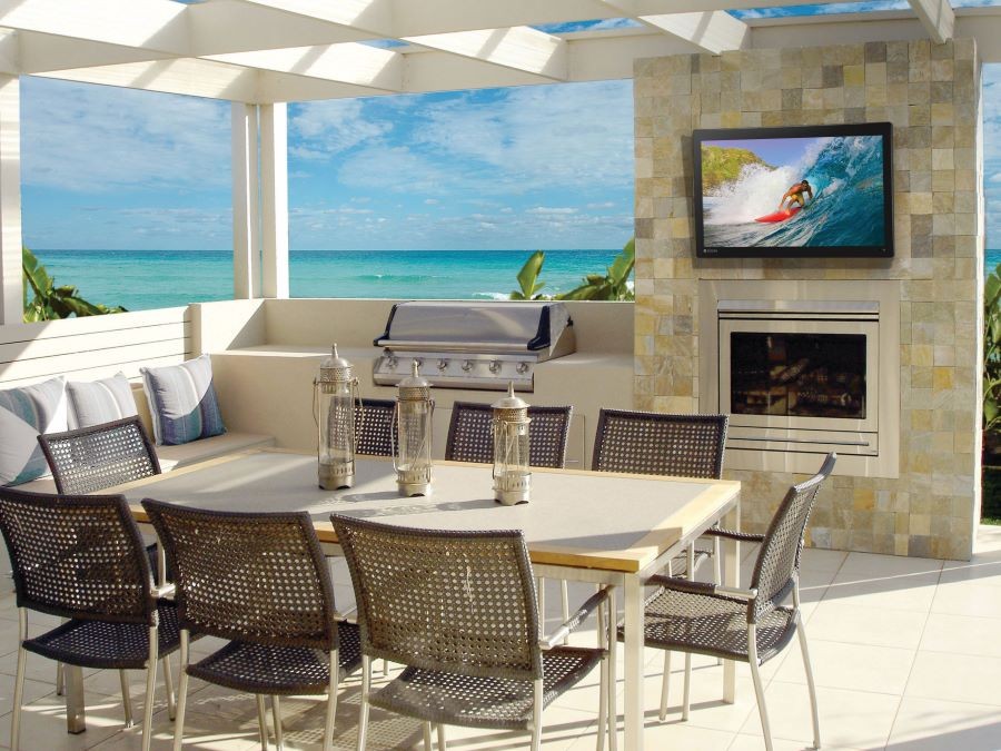  A Seura Storm outdoor TV on a patio above a fireplace next to a grill.